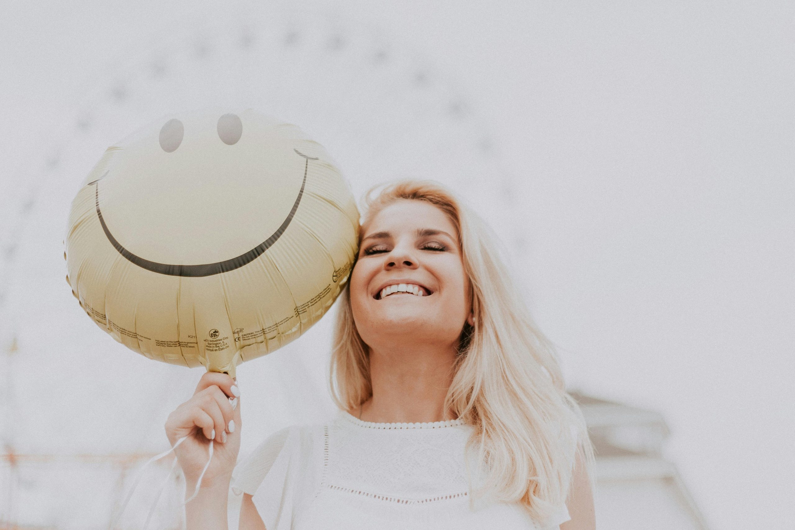 A woman holding a ballon with a smiley face on it. The woman is smiling.